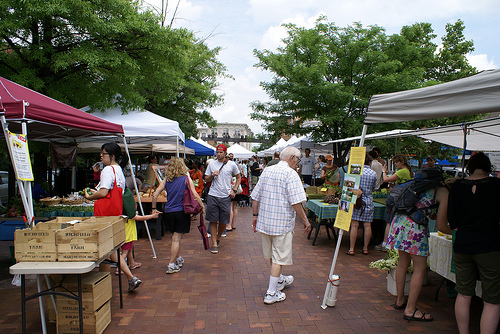 Rows of tents with picnic tables under them line each side of a red brick aisle. People are clustered looking at the wares on the tables, or walking through the aisle.